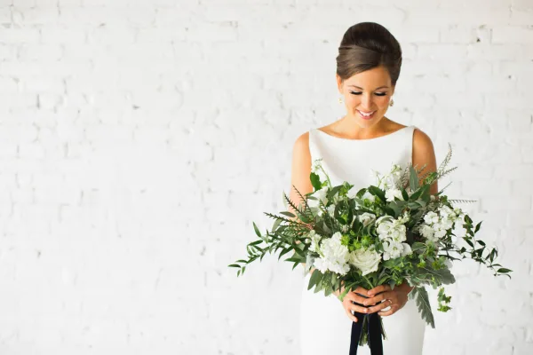 A bride in a white dress holding a large bouquet of white flowers and greenery.