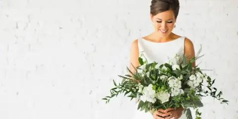 A bride in a white dress holding a large bouquet of white flowers and greenery.