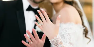 A bride and groom smiling at the camera, with the bride holding up her hand to show her wedding ring.