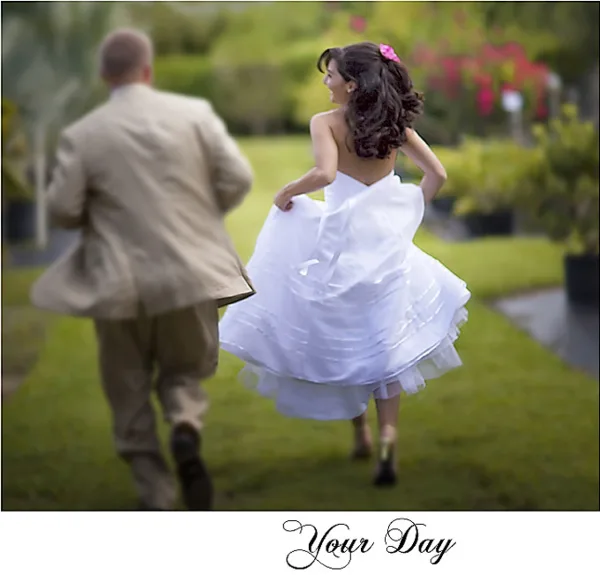 A bride in a white dress and a groom in a tan suit walking through a garden.