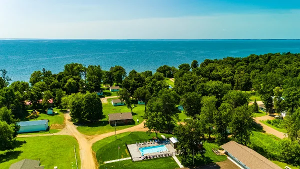 Aerial view of a lakeside resort with cabins, green lawns, a swimming pool, and a large lake in the background.