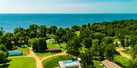 Aerial view of a lakeside resort with cabins, green lawns, a swimming pool, and a large lake in the background.