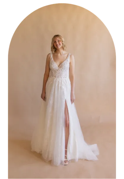 Bride in a white lace wedding gown standing before a soft beige backdrop
