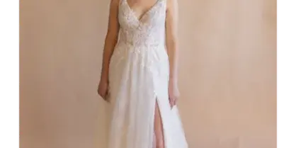 Bride in a white lace wedding gown standing before a soft beige backdrop