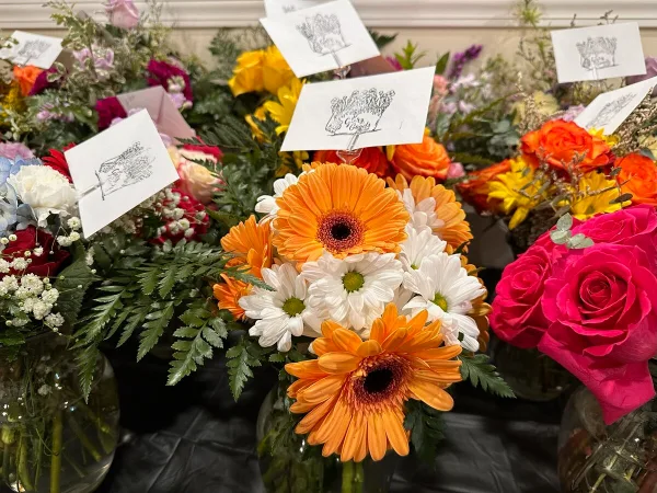 A collection of colorful flower arrangements featuring orange gerbera daisies, white daisies, and pink roses, with small branded cards attached.