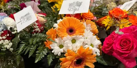 A collection of colorful flower arrangements featuring orange gerbera daisies, white daisies, and pink roses, with small branded cards attached.