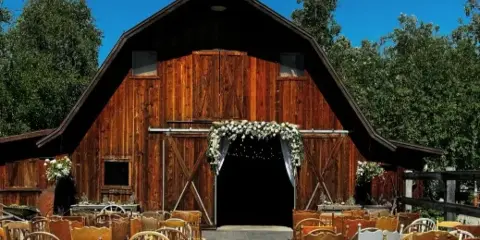 A wedding ceremony setup with rows of wooden chairs and a floral arch in front of a rustic wooden barn.