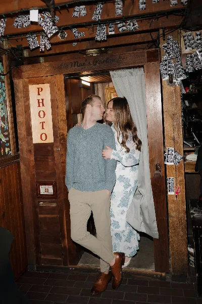 A couple embracing in a rustic wooden doorway with a 'PHOTO' sign, illustrating a lifestyle photography session.