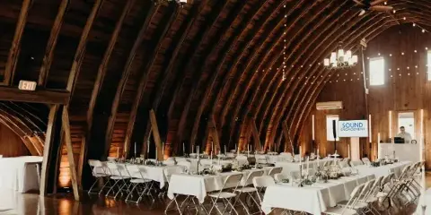 Interior view of a rustic wooden event venue with arched ceilings, chandeliers, and set reception tables.