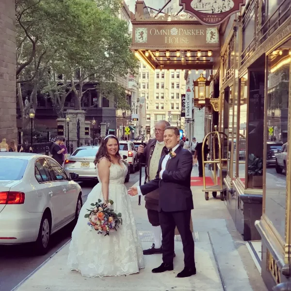 A bride and groom posing on a city street in front of a hotel entrance.