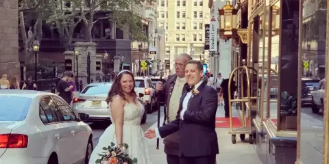 A bride and groom posing on a city street in front of a hotel entrance.