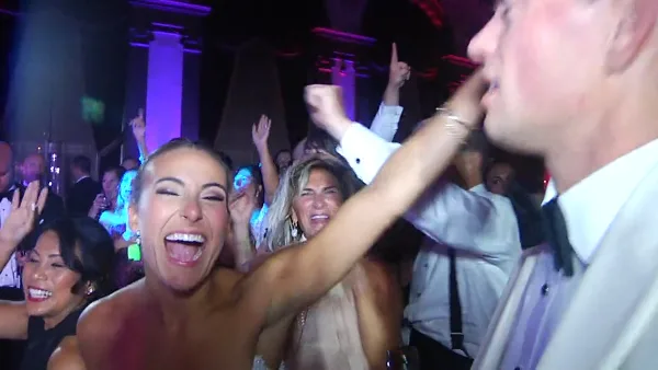 Guests dancing and celebrating at a wedding reception with colorful lighting.