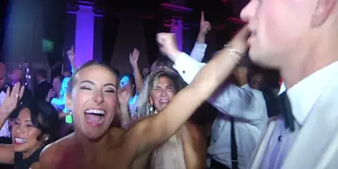 Guests dancing and celebrating at a wedding reception with colorful lighting.