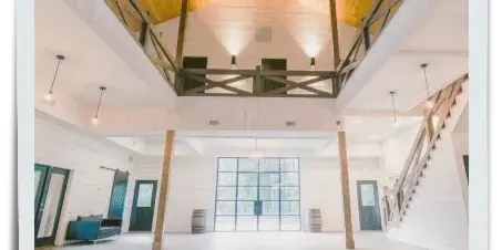 Interior view of a modern rustic event venue with high wooden ceilings and white walls.