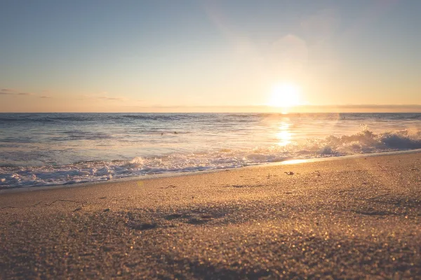 Sunset over a calm ocean with waves washing onto a sandy beach