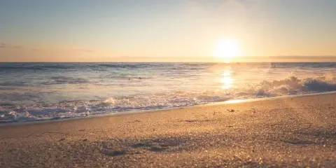 Sunset over a calm ocean with waves washing onto a sandy beach