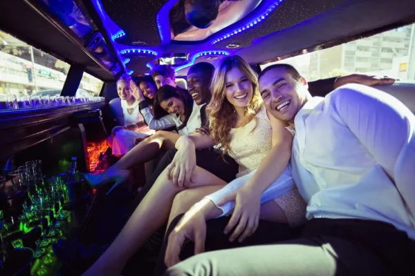 Passengers seated inside a luxury limousine with blue LED lighting and a bar area.