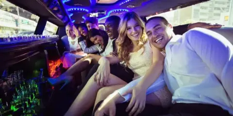 Passengers seated inside a luxury limousine with blue LED lighting and a bar area.