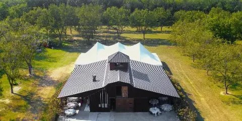 Aerial view of a large barn-style event venue with a white tent and set-up tables on a grassy estate.