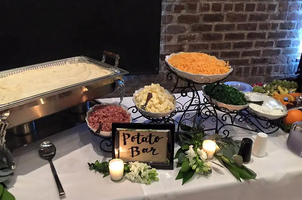 Catering buffet table with chafing dishes, potato bar sign, and assorted side dishes