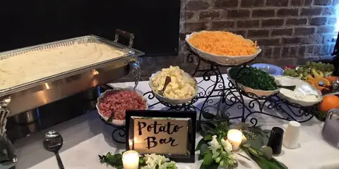 Catering buffet table with chafing dishes, potato bar sign, and assorted side dishes