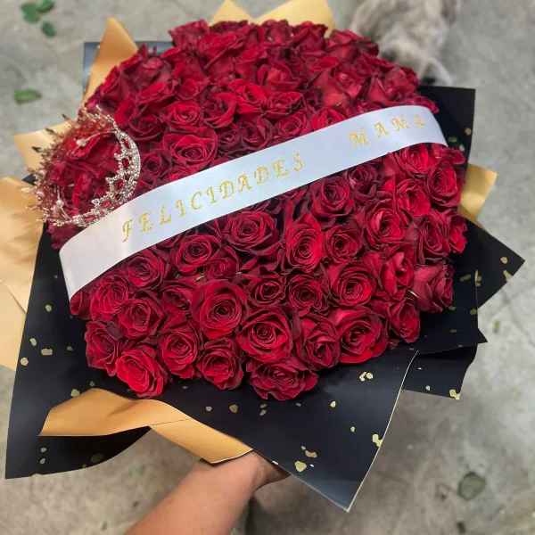 A large bouquet of red roses wrapped in black and gold paper with a white ribbon reading 'FELICIDADES MAMA'