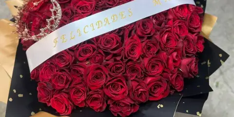 A large bouquet of red roses wrapped in black and gold paper with a white ribbon reading 'FELICIDADES MAMA'