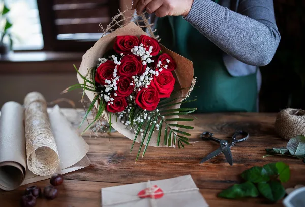 A florist arranging a bouquet of red roses and white baby's breath on a wooden workbench.