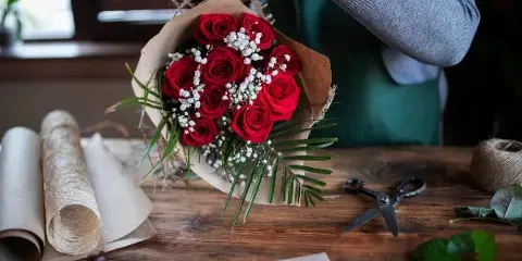 A florist arranging a bouquet of red roses and white baby's breath on a wooden workbench.