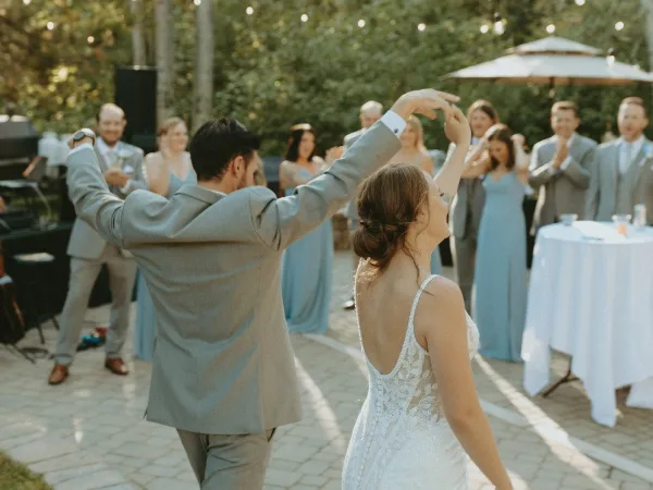 A bride and groom dancing at an outdoor wedding reception while guests in formal attire watch and applaud.
