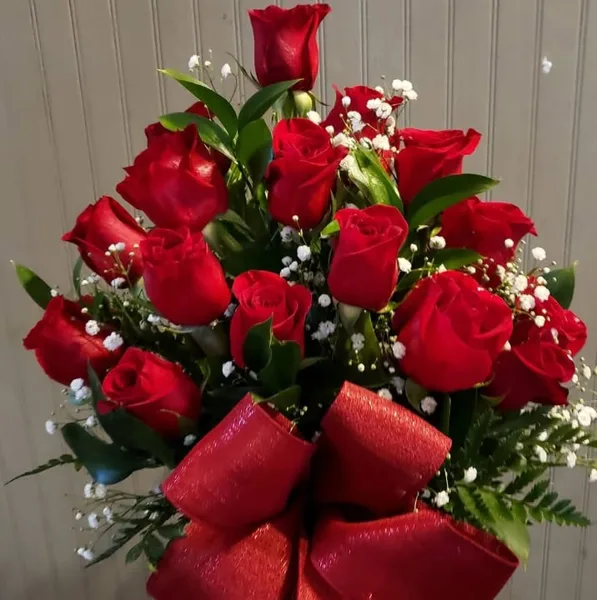 A bouquet of fresh red roses with green leaves and a large red bow.