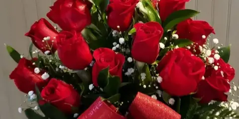 A bouquet of fresh red roses with green leaves and a large red bow.