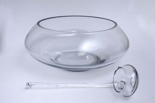 A clear glass punch bowl with a matching glass ladle resting on a white surface.