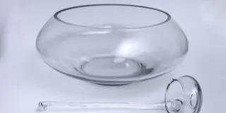 A clear glass punch bowl with a matching glass ladle resting on a white surface.