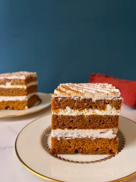 A slice of layered cake with white frosting served on a white plate with a gold rim.