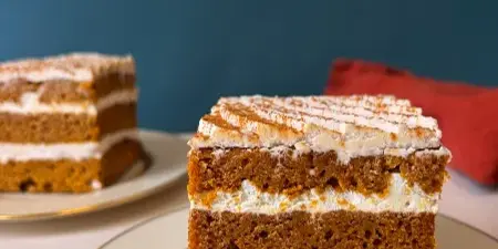 A slice of layered cake with white frosting served on a white plate with a gold rim.