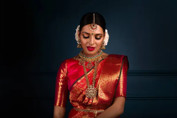 A bride with professional makeup and styled hair, wearing traditional Indian bridal attire and jewelry.