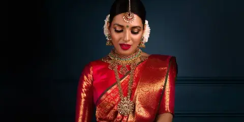 A bride with professional makeup and styled hair, wearing traditional Indian bridal attire and jewelry.