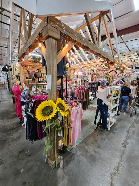 Interior view of The Dallas Markets showing a vendor booth with clothing racks, mannequins, and sunflower decorations.
