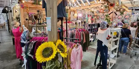 Interior view of The Dallas Markets showing a vendor booth with clothing racks, mannequins, and sunflower decorations.