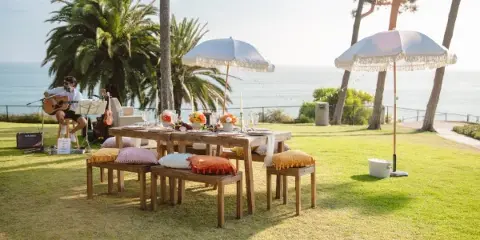 A professionally styled outdoor event table with a live musician playing guitar on a lawn near the ocean.