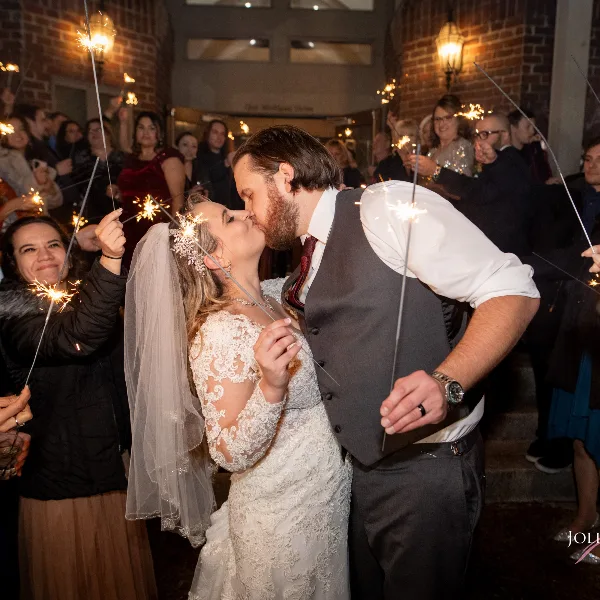 A bride and groom kissing during a sparkler exit at a wedding venue, surrounded by guests.