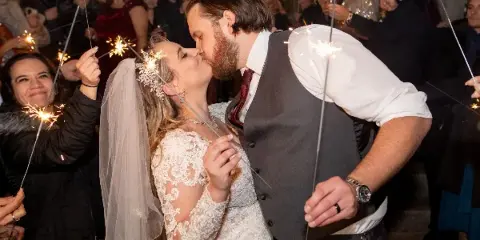 A bride and groom kissing during a sparkler exit at a wedding venue, surrounded by guests.