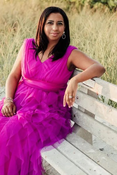 Portrait of Nailah, the owner of One Stop Wedding Shop, wearing a pink dress and sitting on a bench.