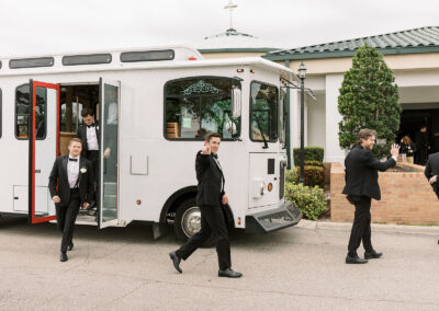 A white trolley parked outside a venue with a groom and groomsmen in black suits standing nearby.