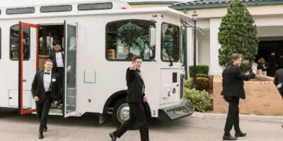 A white trolley parked outside a venue with a groom and groomsmen in black suits standing nearby.