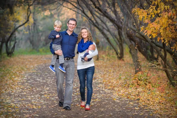 A professional portrait of a family of four walking on a path in an autumn forest.