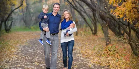 A professional portrait of a family of four walking on a path in an autumn forest.