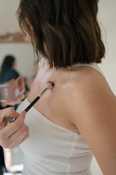 A makeup artist applying product to a client's shoulder with a brush.