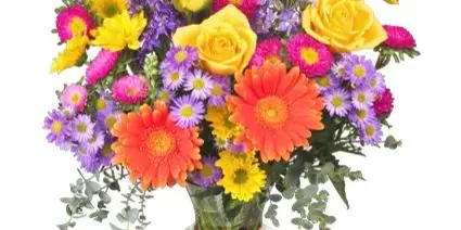 A colorful floral bouquet featuring yellow roses, orange gerbera daisies, and purple asters arranged in a clear glass vase.
